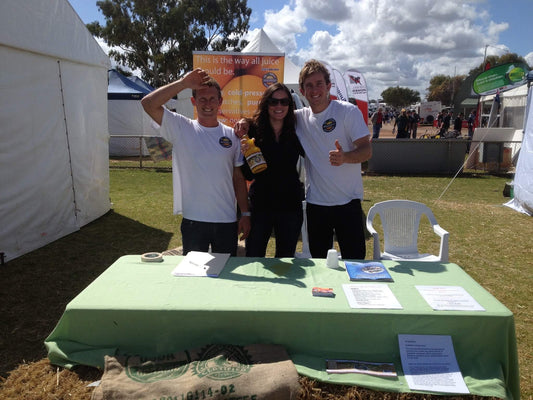 Two Funk Drinks Co team members in white polo shirts and a colleague holding a bottle of cold pressed juice at an early outdoor market stall, in front of a Funk juice banner