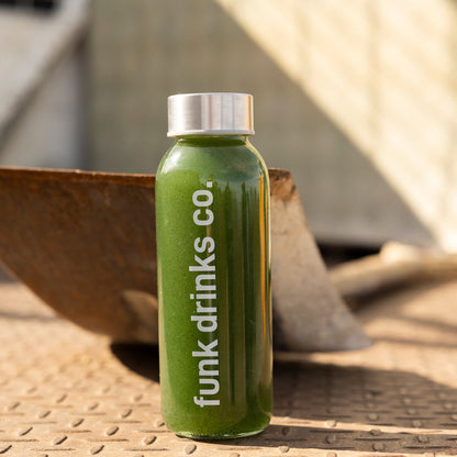 Funk Drinks Co Living Green cold pressed juice bottle, bright green, on a metal surface beside a shovel