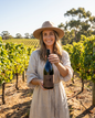 A woman in a wide brim hat holding a bottle of Funk 108 Shiraz among the vines in the Swan Valley
