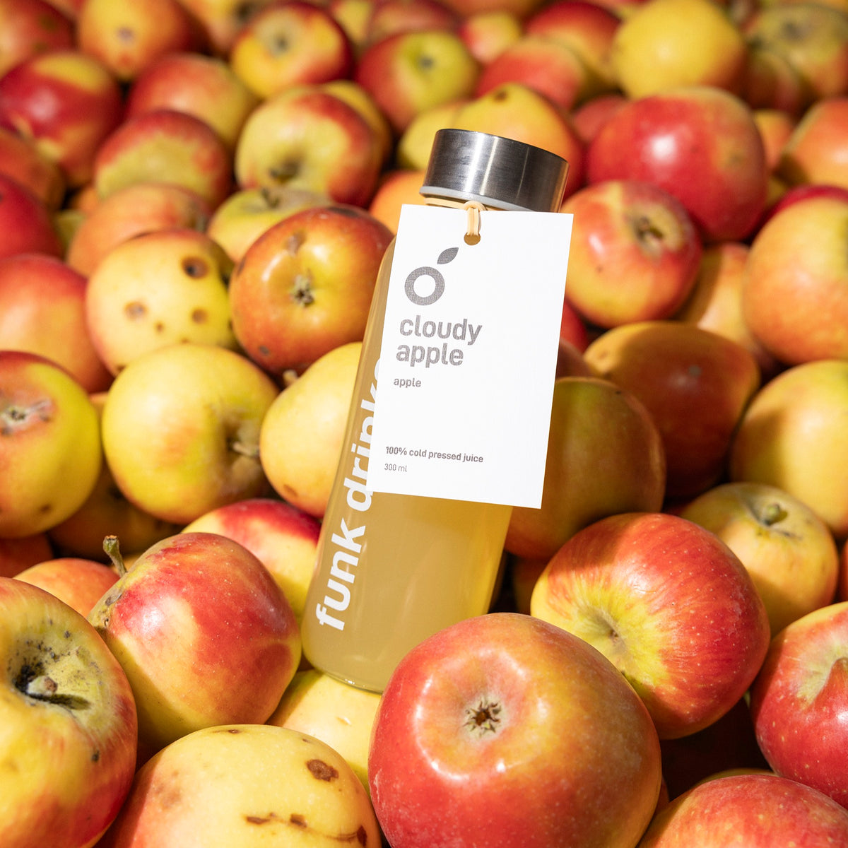A tagged bottle of Funk Cloudy Apple cold pressed juice sitting in a crate of apples