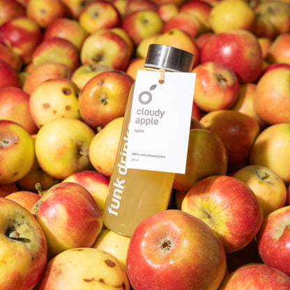 A tagged bottle of Funk Cloudy Apple cold pressed juice sitting in a crate of apples