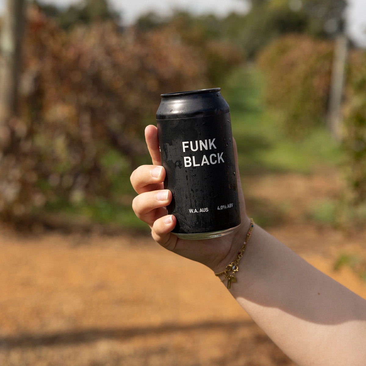 A hand holding a can of Funk Black dark ale in front of the vines