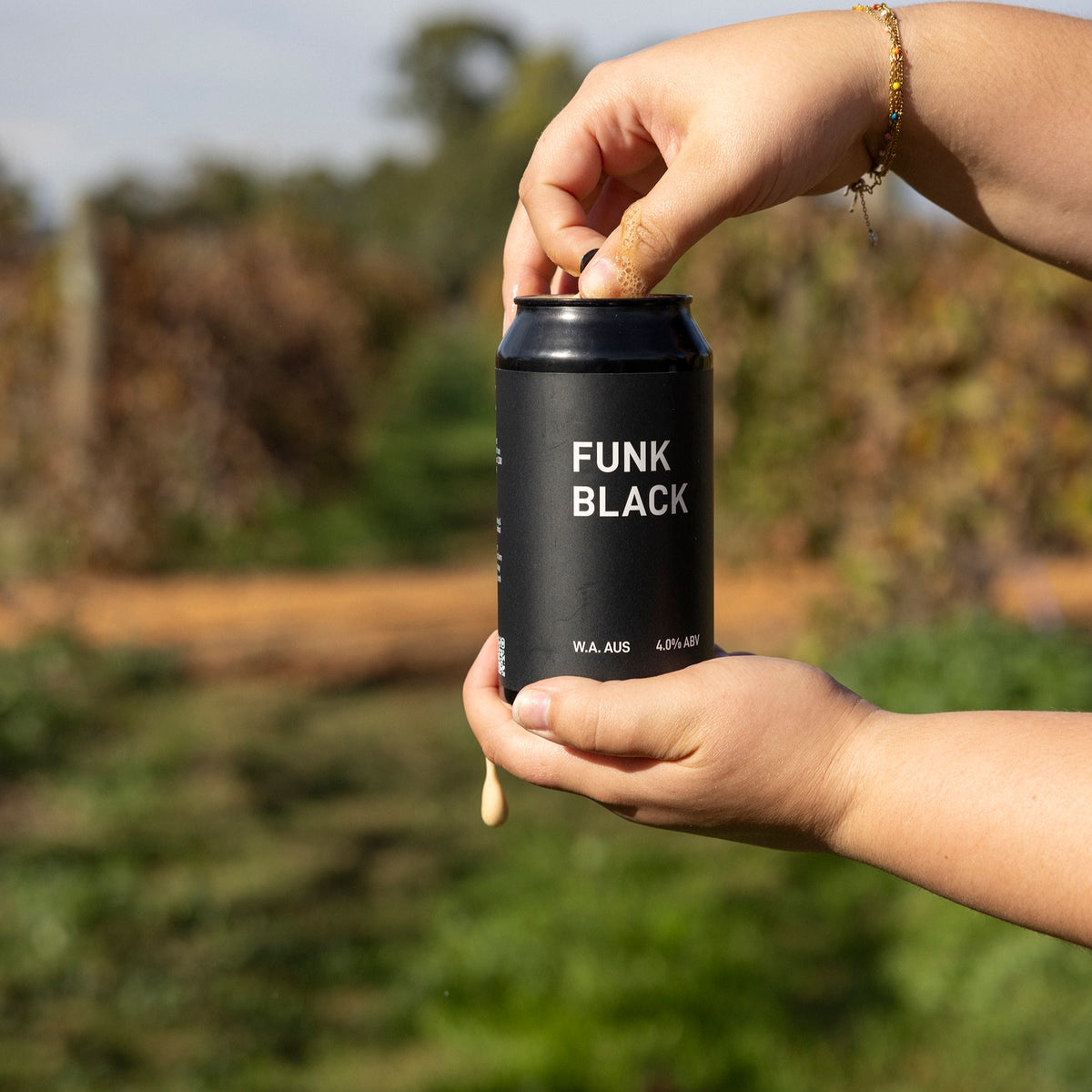 Two hands cracking open a can of Funk Black dark ale outdoors