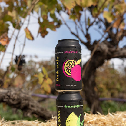 Cans of Funk Passionfruit and Lemon Ginger craft soda stacked on a straw bale