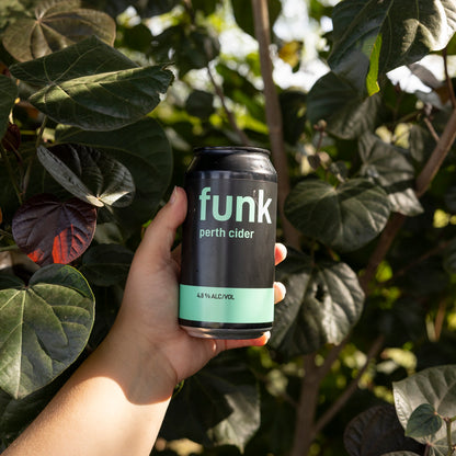 A hand holding a can of Funk Perth Cider among green leaves